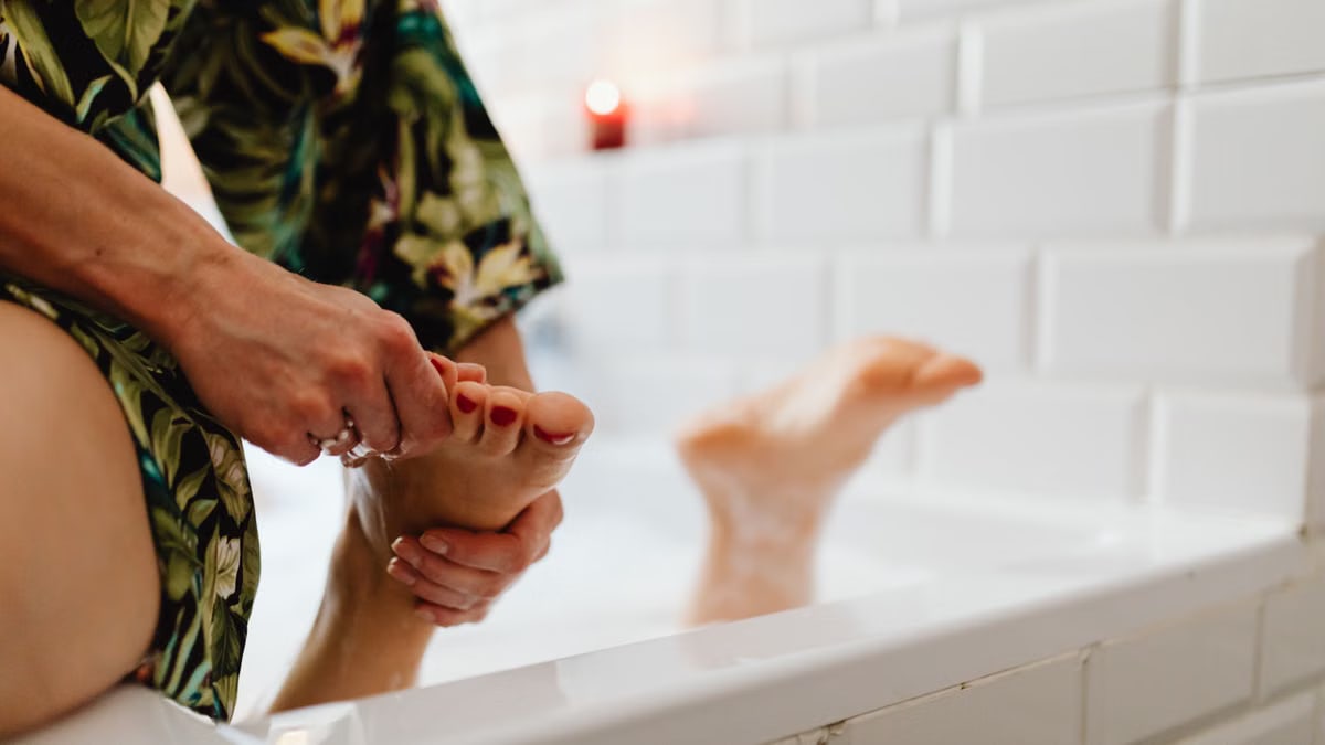 A soothing foot massage being given in a bath with white tiled walls and a relaxed atmosphere.